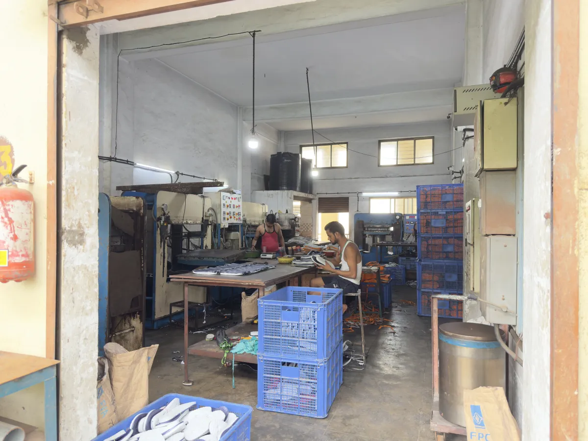 Workers trimming and pairing footwear at benches on the Arbuda Plastic factory floor