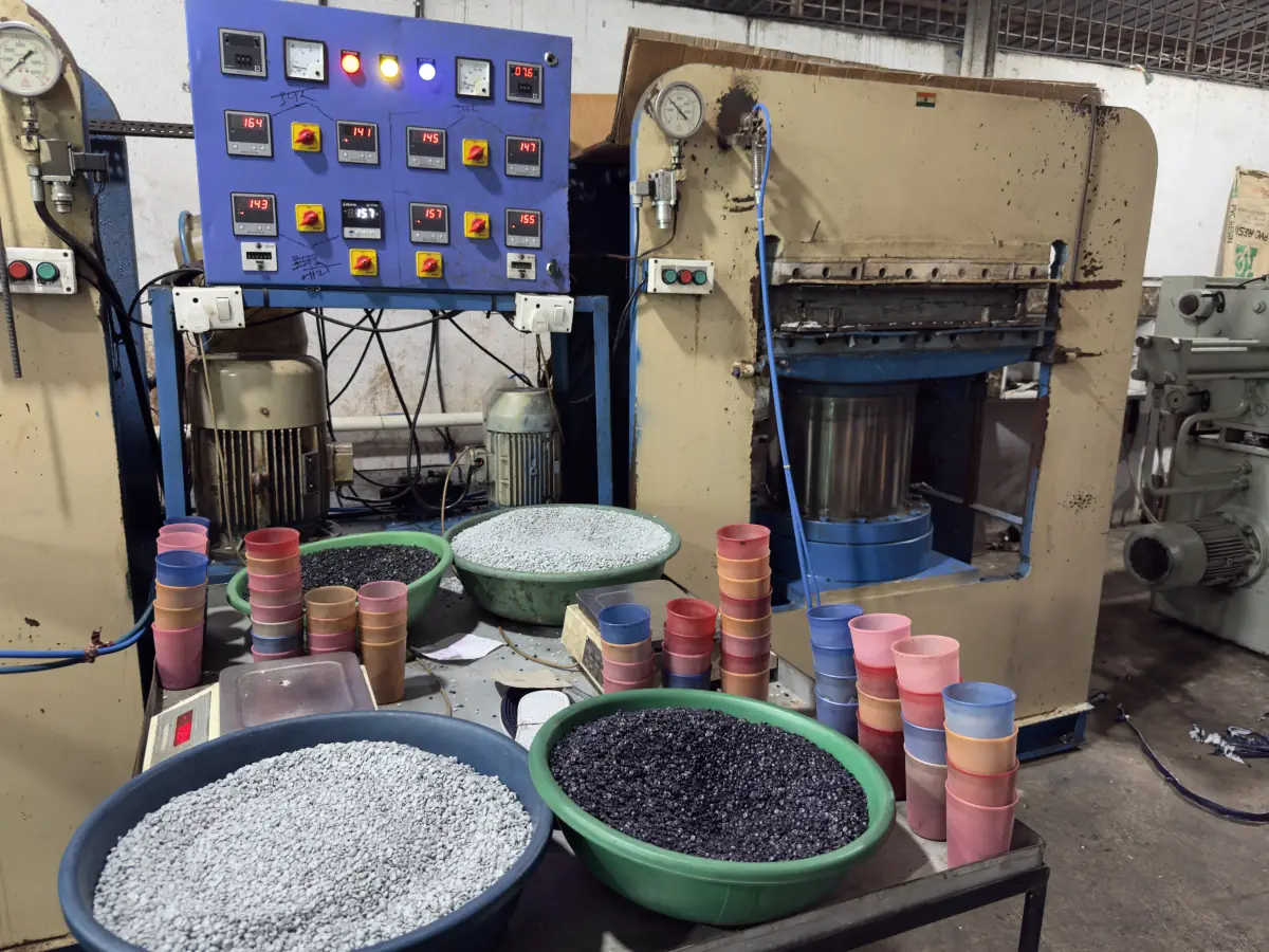 Basins of grey and black PVC granules with colour-measuring cups beside a hydraulic press control panel