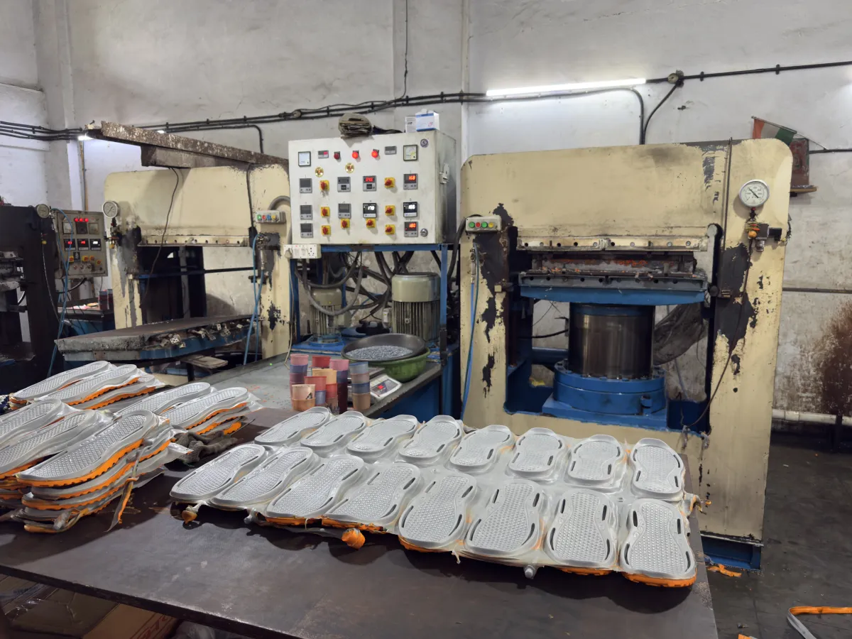 Freshly moulded grey and orange EVA soles laid out in front of two hydraulic press machines